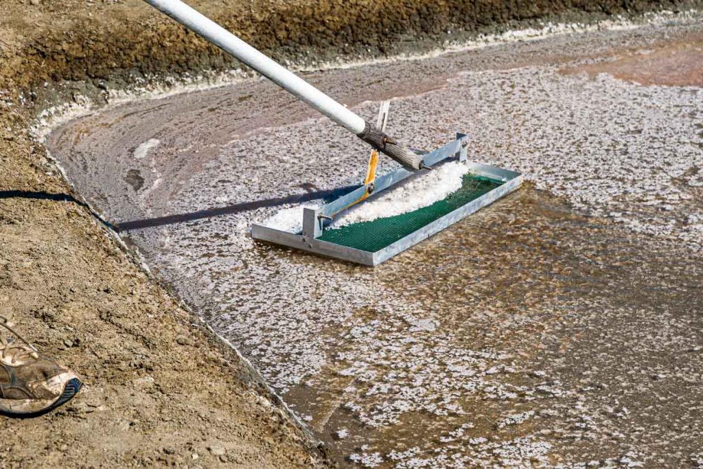 Die Salzflocken werden vorsichtig von der Wasseroberfläche geschöpft. Dabei darf das Werkzeug im flachen Becken nicht mit dem Lehmboden in Berührung kommen / © Foto: Georg Berg