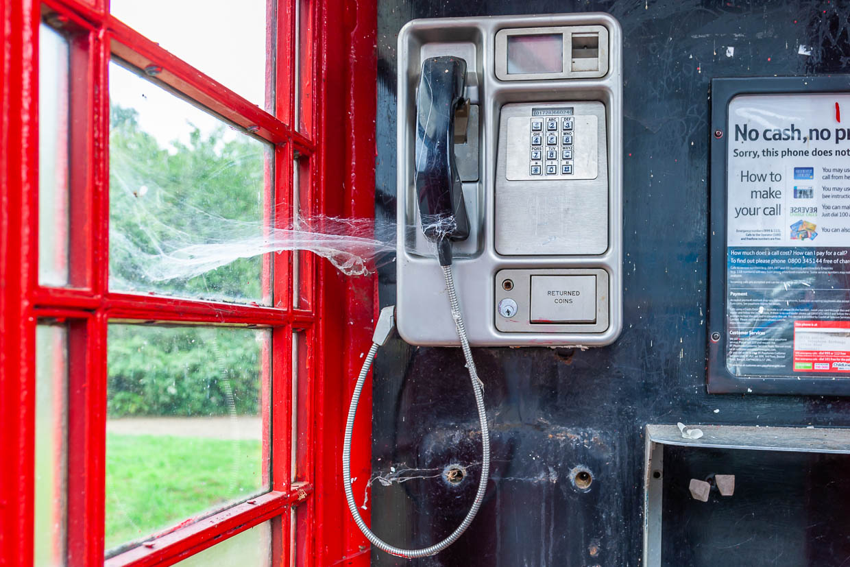 A traditional red telephone booth in a rural setting in the United Kingdom features a spider web above the receiver / © Photo: Georg Berg