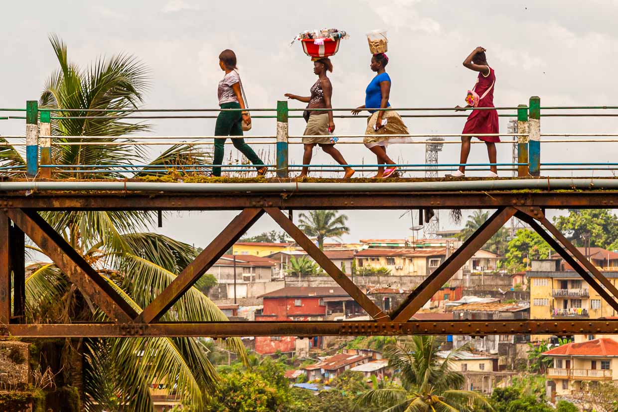 Women cross Freetown's old railroad bridge, the Tengbeh Bridge, carrying goods on their heads / © Photo: Georg Berg
