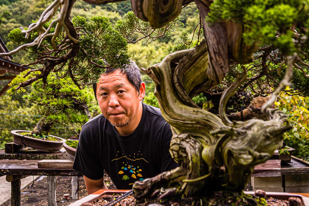 Bonsai master and garden owner Toshio Ohsugi in portrait with a 500-year-old care case. According to records, the tree was taken from a rock in the mountains around 1920. Its roots had driven a fissure into the rock / © Photo: Georg Berg