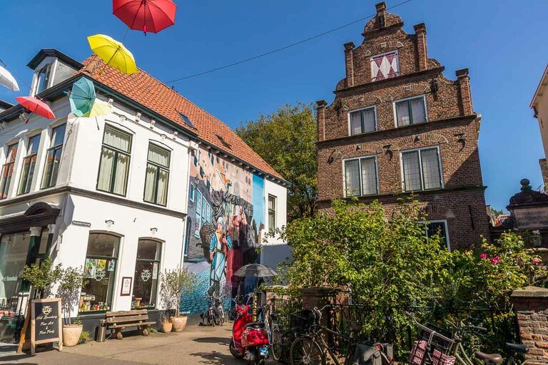 Mural painting in the old town of Deventer. Motif on the occasion of the Hanseatic Year, which the nine Hanseatic cities of Holland celebrate in 2023. The mural has a reference to the past and present. Here in Deventer: Market woman with son selling Deventer honey cake and stockfish, important goods in the Hanseatic trade of Deventer. The boy wears a fan scarf of the soccer club Deventer Eagles / © Photo: Georg Berg